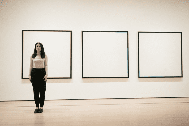 Woman standing in front of three white canvases with dark outlines mounted on a white wall.