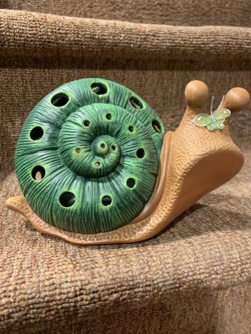 Ceramic snail with a tan body and Green shell. There are little holes in the shell to allow light to poke through