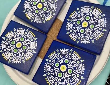 Photo of four square coasters, painted a dark blue with an intricate circular pattern painted in white