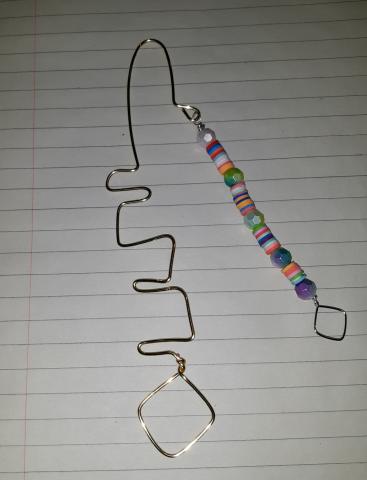 on a white background, there is an image of a bookmark bent in a serpentine formation, with a strand of colorful beads hanging off of the top
